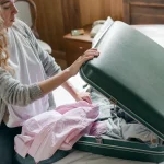 person closing a hard-shell suitcase on a bed