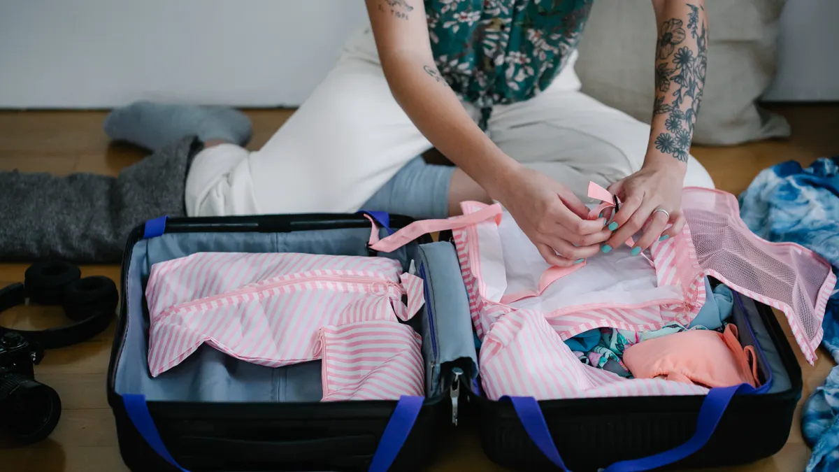 person packing clothes into an open suitcase on the floor